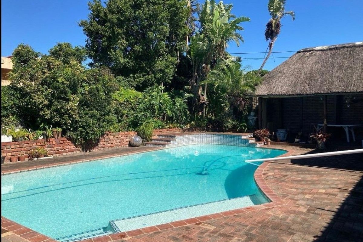 Outdoor pool area featuring a swimming pool with tiled steps, brick paving surround, and an adjacent thatched lapa structure.