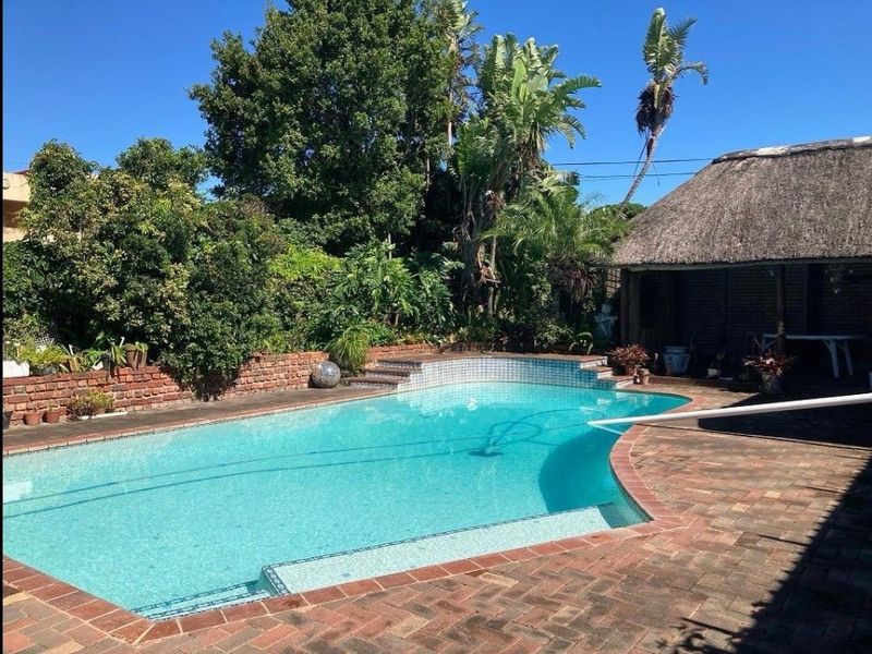 Outdoor pool area featuring a swimming pool with tiled steps, brick paving surround, and an adjacent thatched lapa structure.