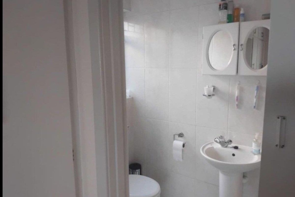 A functional bathroom featuring a pedestal sink, wall-mounted medicine cabinet, and toilet with neutral wall tiling.
