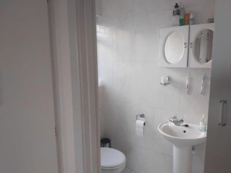 A functional bathroom featuring a pedestal sink, wall-mounted medicine cabinet, and toilet with neutral wall tiling.