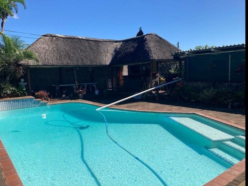 Outdoor pool area featuring a swimming pool with a paved deck and an adjacent thatched roof lapa with a built-in braai.