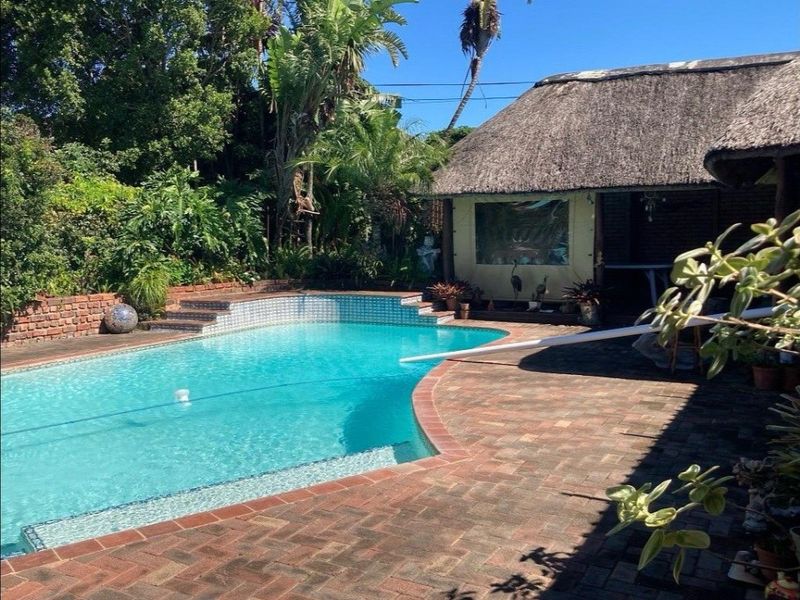 Outdoor pool area featuring a swimming pool, brick paving, and an adjacent thatched roof structure set within a landscaped garden.