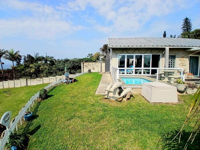 Rear exterior view featuring a swimming pool, paved patio area, and a well-maintained lawn with boundary walling and distant coastal views.