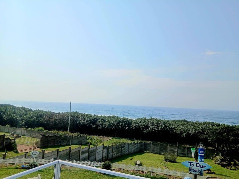 Elevated coastal view overlooking a private garden, boundary fencing, and the ocean horizon.
