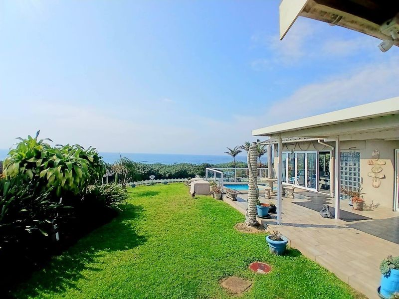 Rear exterior view featuring a covered patio, swimming pool, and landscaped garden with expansive ocean views.