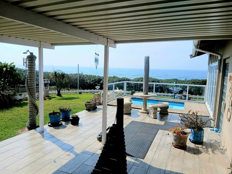 A spacious covered patio featuring tiled flooring, overlooking a private swimming pool and offering expansive ocean views.