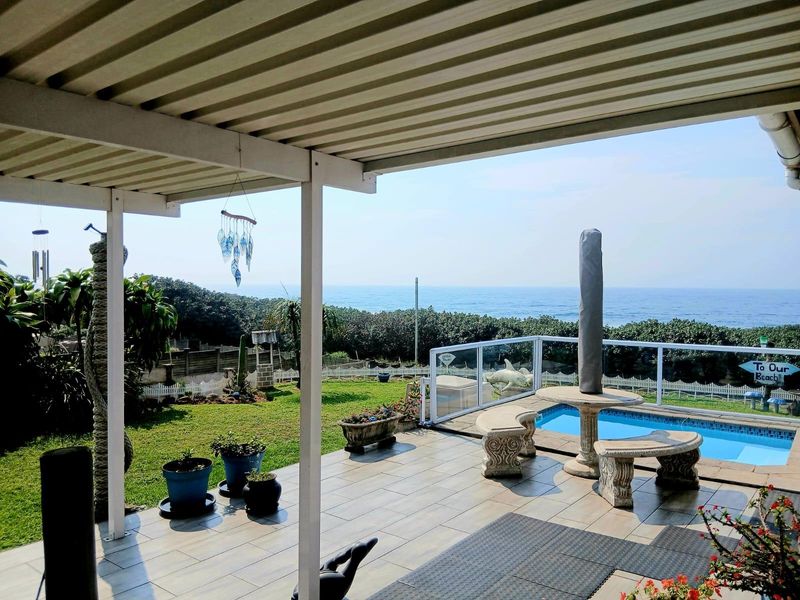 Covered patio area featuring tiled flooring and glass balustrades, overlooking a private swimming pool with expansive ocean views.