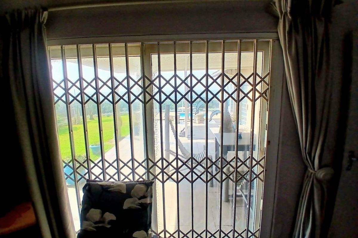 A living room view looking out through a sliding glass door protected by a metal security gate towards a garden and pool area.