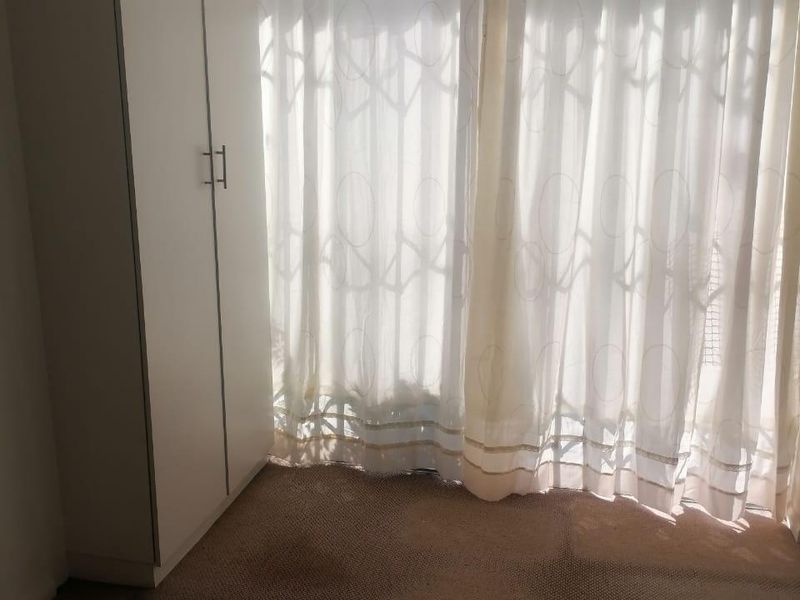 A vacant bedroom featuring built-in wardrobe storage and carpeted flooring, with natural light filtering through window curtains.
