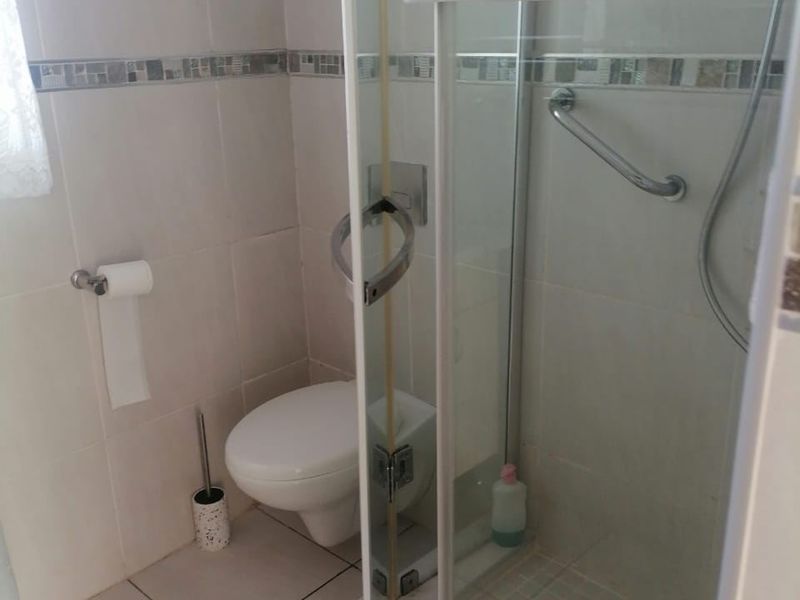 A functional bathroom featuring a corner shower enclosure with a grab rail, wall-mounted toilet, and neutral tiled finishes.