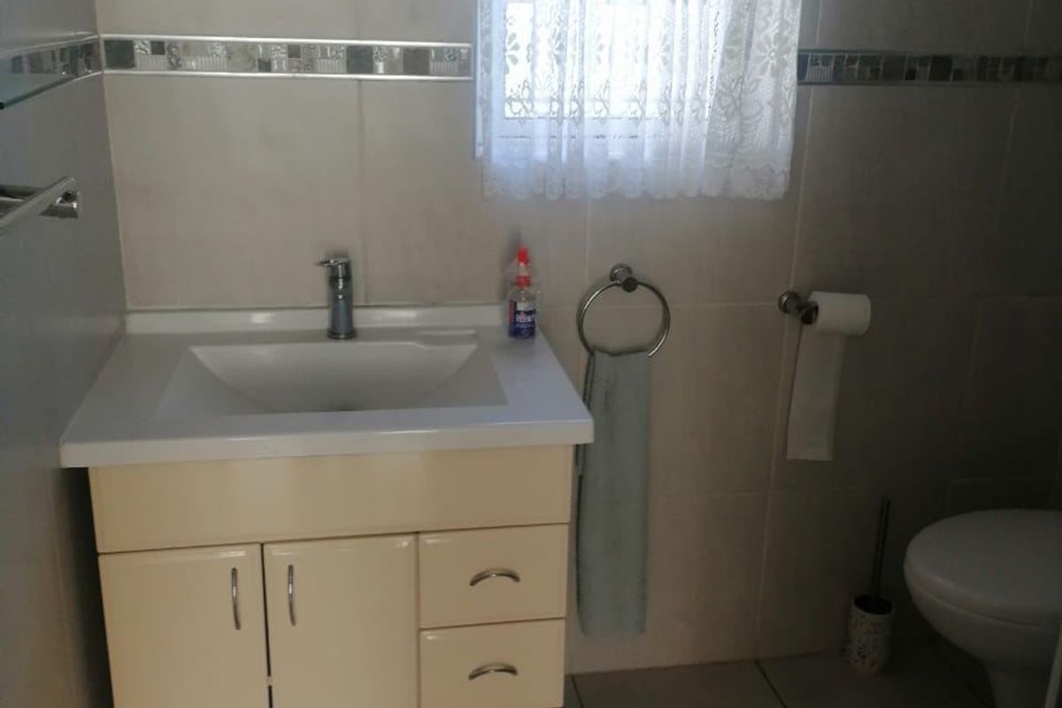 A functional bathroom featuring a vanity cabinet with integrated basin, tiled walls and flooring, and standard sanitary fixtures.