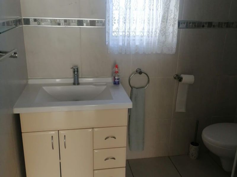 A functional bathroom featuring a vanity cabinet with integrated basin, tiled walls and flooring, and standard sanitary fixtures.