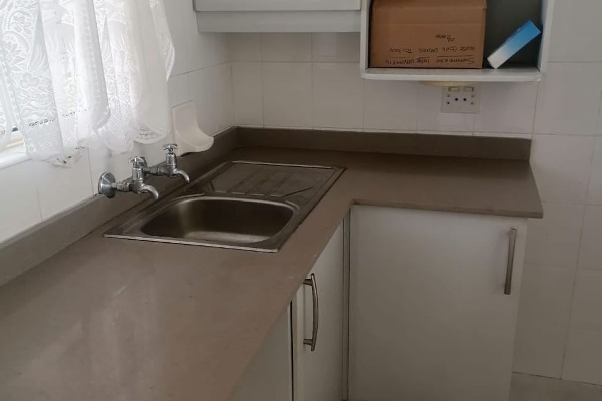 A compact kitchen area featuring built-in cabinetry, a stainless steel sink with mixer tap, laminate countertops, and tiled splashbacks.