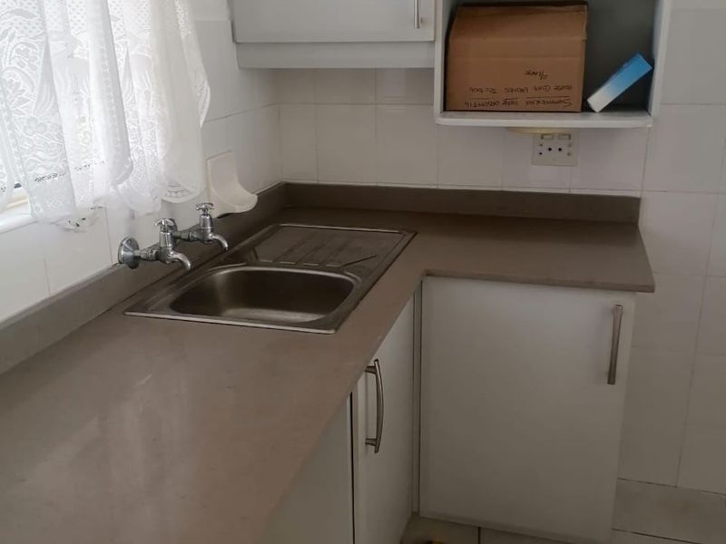 A compact kitchen area featuring built-in cabinetry, a stainless steel sink with mixer tap, laminate countertops, and tiled splashbacks.