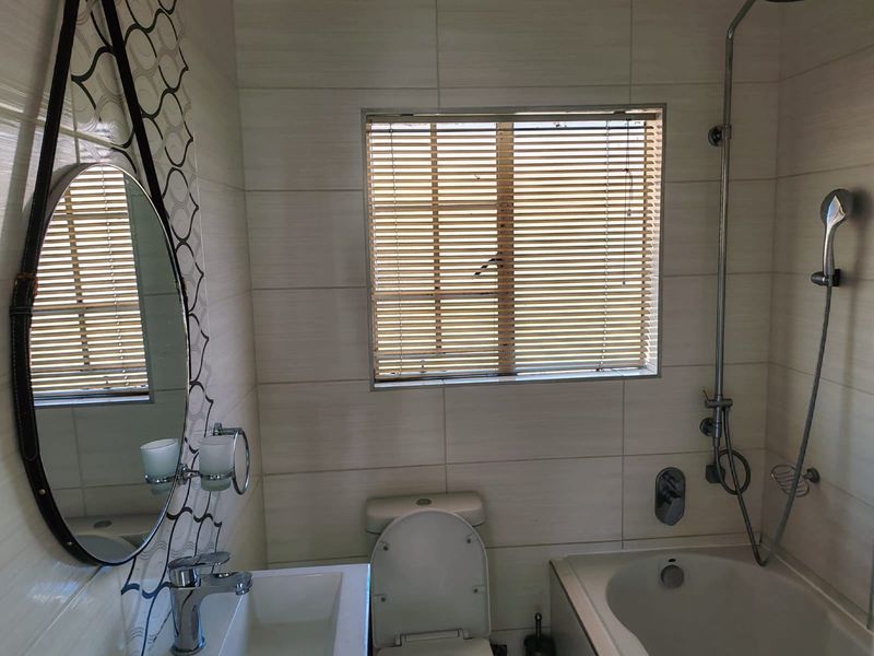 A functional bathroom featuring a built-in bathtub with shower attachment, a modern vanity basin, and neutral wall tiling.