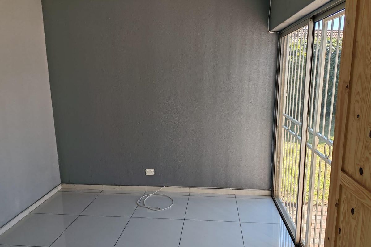 An empty living room featuring tiled flooring and a sliding glass door with a security gate, providing direct access to the outdoor area.