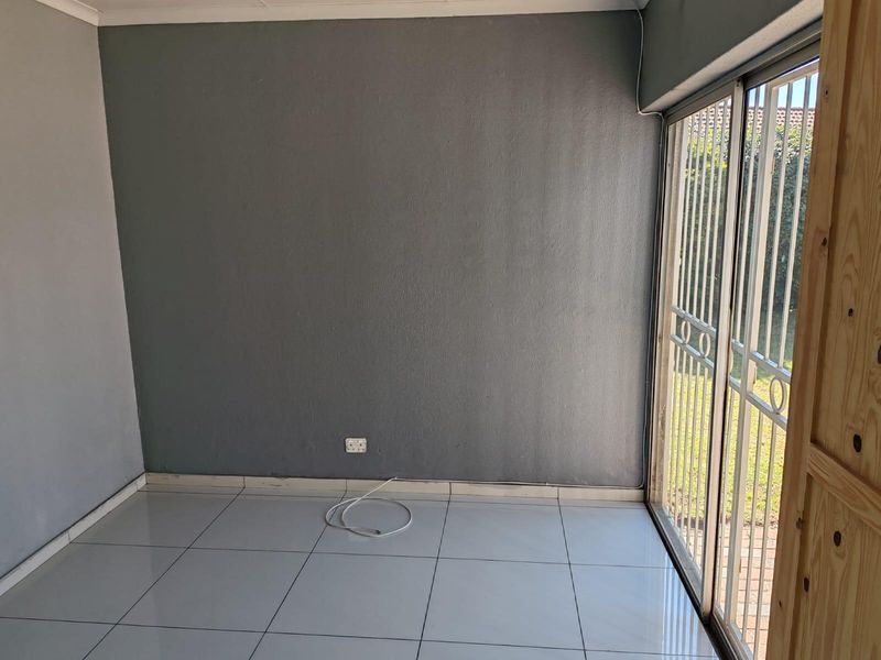An empty living room featuring tiled flooring and a sliding glass door with a security gate, providing direct access to the outdoor area.