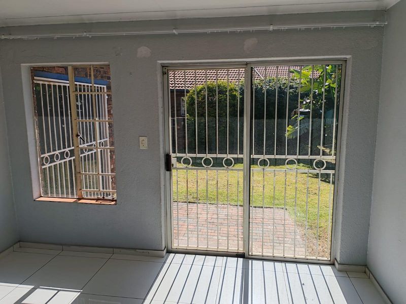 An empty living area featuring tiled floors, security bars on the window, and a sliding door leading to the rear garden.