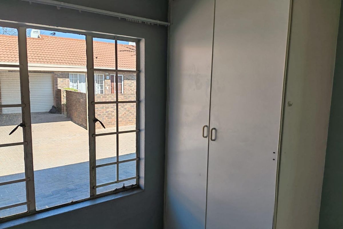 A vacant bedroom featuring a built-in wardrobe and a steel-framed window overlooking the exterior driveway area.