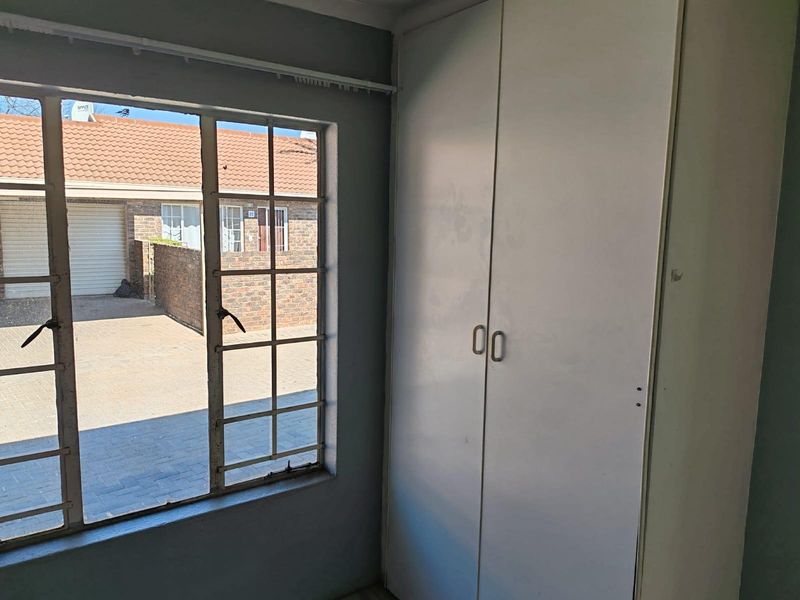 A vacant bedroom featuring a built-in wardrobe and a steel-framed window overlooking the exterior driveway area.