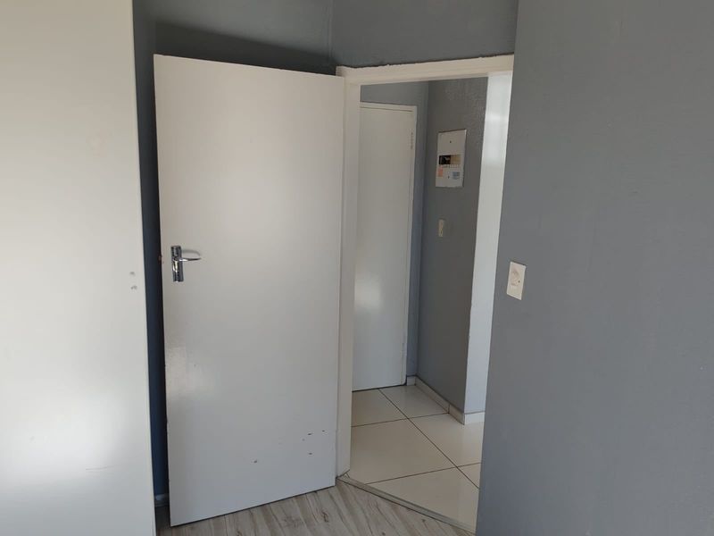 A functional hallway connecting interior spaces, featuring a mix of tiled and laminate flooring with neutral grey wall finishes.