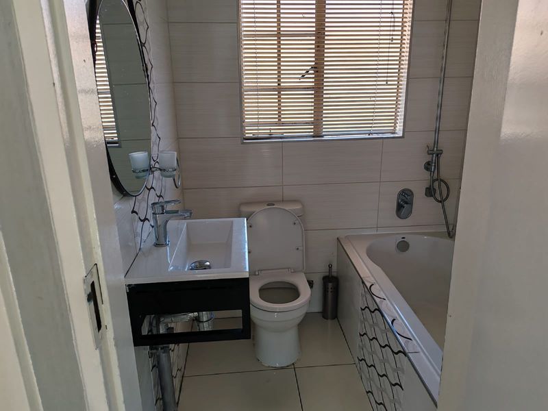A compact, modern bathroom featuring a wall-mounted vanity, a bathtub with shower mixer, and neutral tiled finishes.