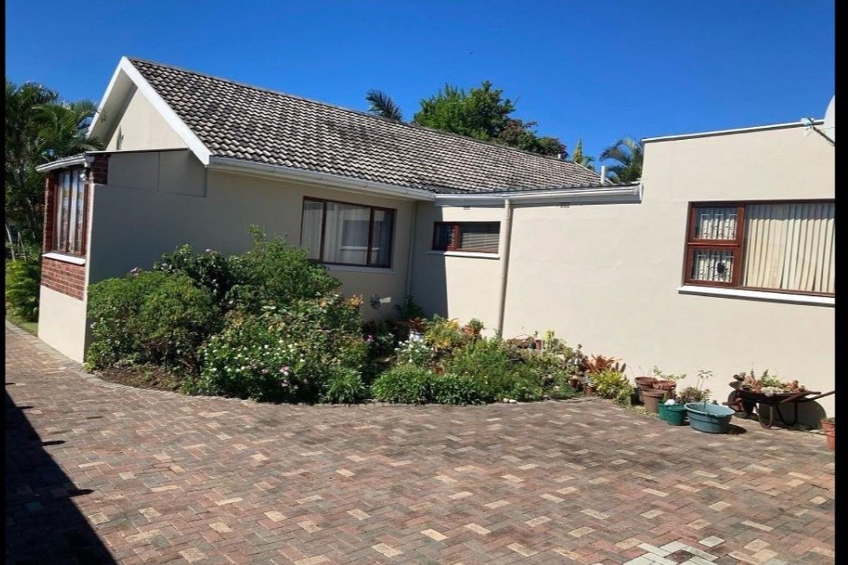 Front exterior view of the house featuring a paved driveway, tiled roof, and established garden beds along the building facade.