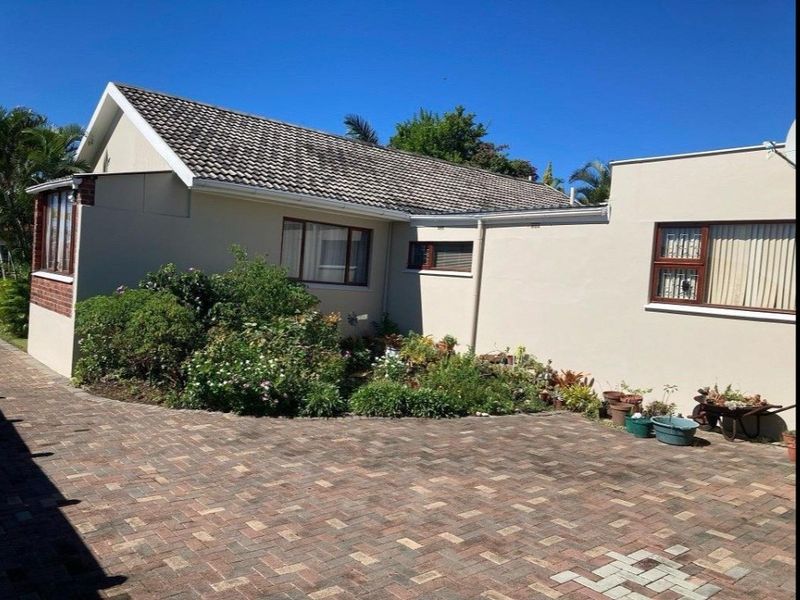 Front exterior view of the house featuring a paved driveway, tiled roof, and established garden beds along the building facade.