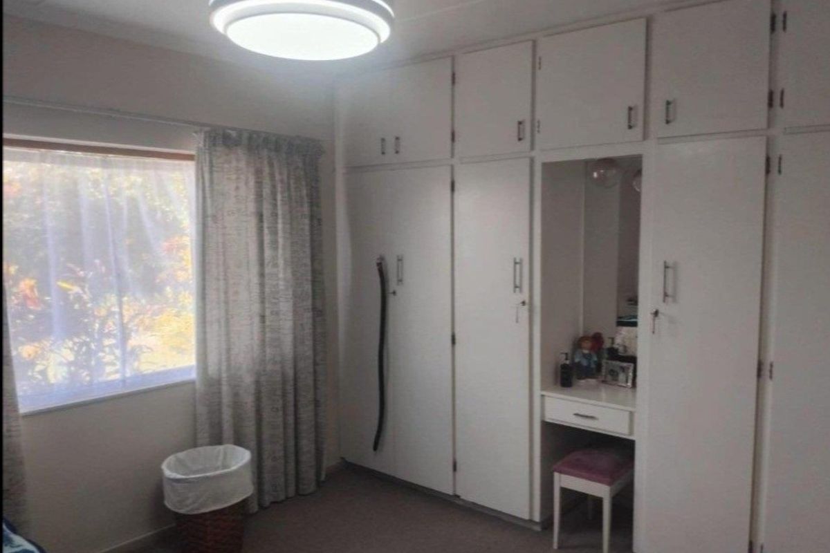 A bedroom featuring extensive white built-in cupboards with an integrated vanity area and a large window providing natural light.