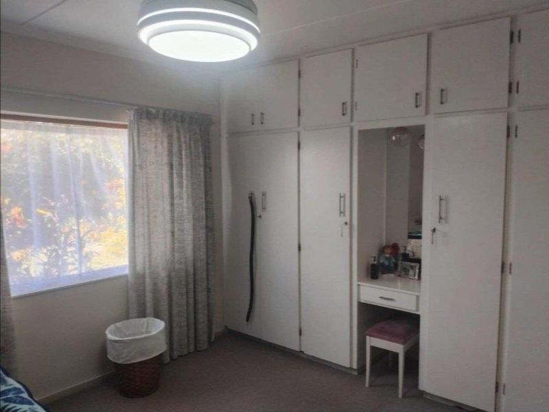 A bedroom featuring extensive white built-in cupboards with an integrated vanity area and a large window providing natural light.