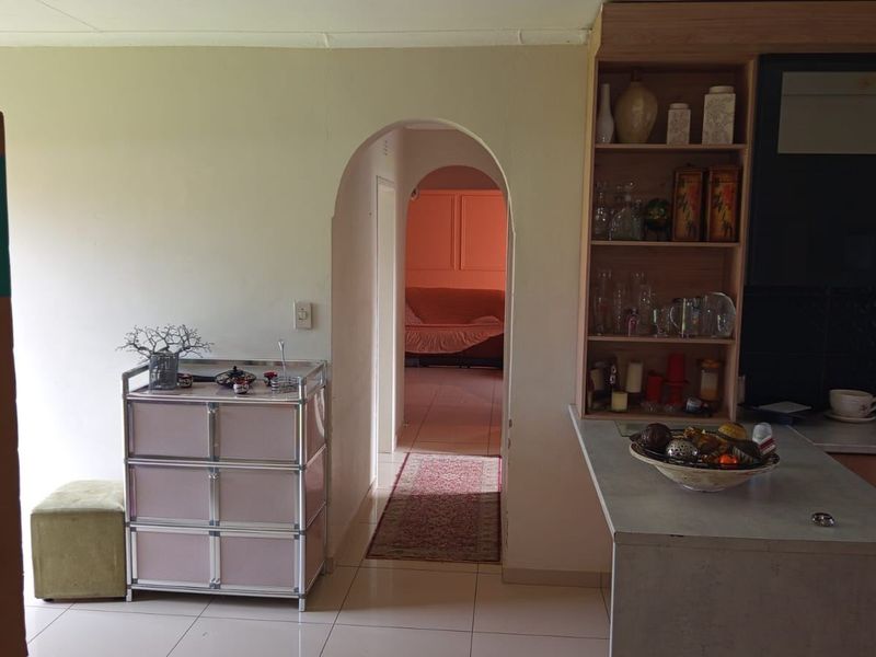 Open plan living area featuring an arched doorway leading to a hallway, tiled flooring, and a built-in kitchen shelving unit.