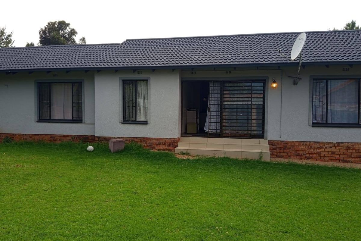Rear view of a single-story house featuring a tiled roof, brick base, and a sliding door entrance leading to a grass lawn.