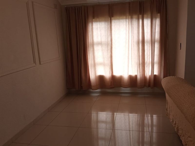 A living room featuring tiled flooring and decorative wall molding, illuminated by natural light through a large window.
