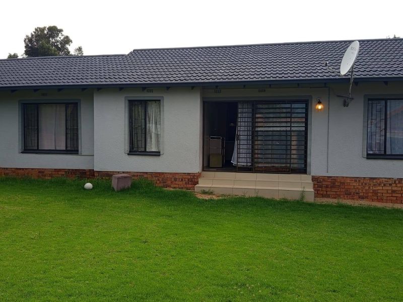 Rear view of a single-story house featuring a tiled roof, brick base, and a sliding door entrance leading to a grass lawn.