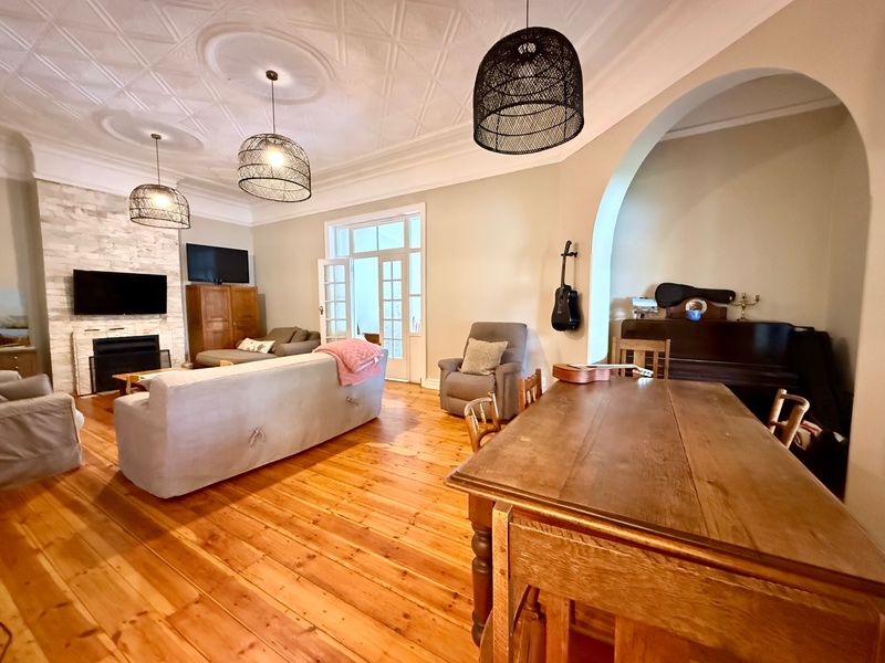 Spacious open-plan living and dining area featuring original hardwood floors, a decorative pressed metal ceiling, and a feature stone-clad fireplace.