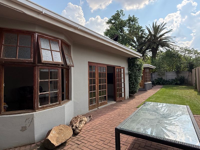 Rear view of the property featuring a brick paved patio, wooden framed bay windows, and french doors leading into the home.