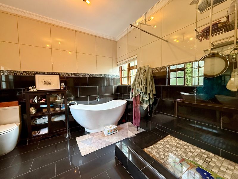 A modern bathroom featuring a freestanding bathtub, a spacious walk-in shower with a glass screen, and high-contrast tiled walls and flooring.