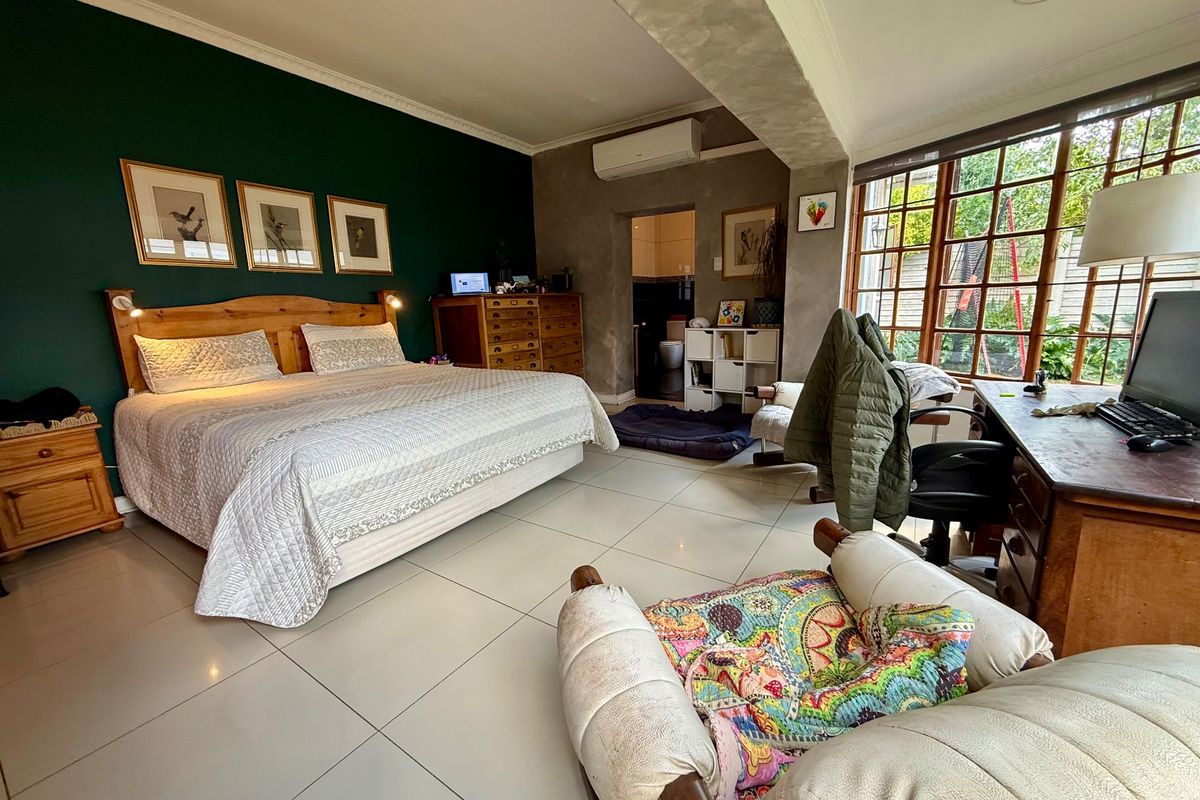 Spacious bedroom featuring tiled flooring, dark green accent wall, split-system air conditioning, and large timber-framed windows with direct access to an en-suite bathroom.