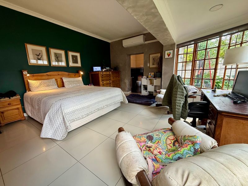 Spacious bedroom featuring tiled flooring, dark green accent wall, split-system air conditioning, and large timber-framed windows with direct access to an en-suite bathroom.