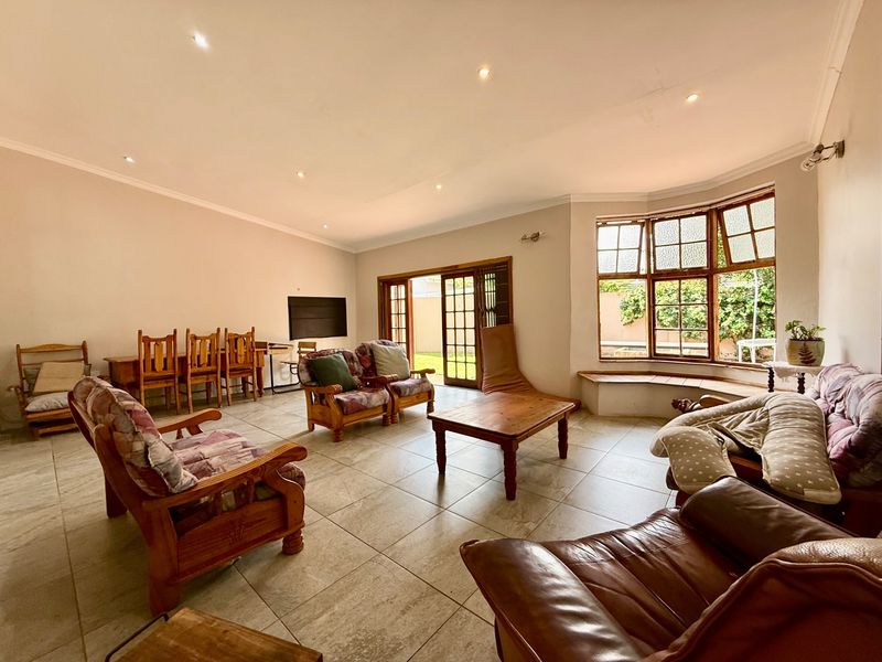 Spacious living room featuring large tiled flooring, recessed downlights, a charming bay window with a built-in seat, and direct access to the garden via french doors.