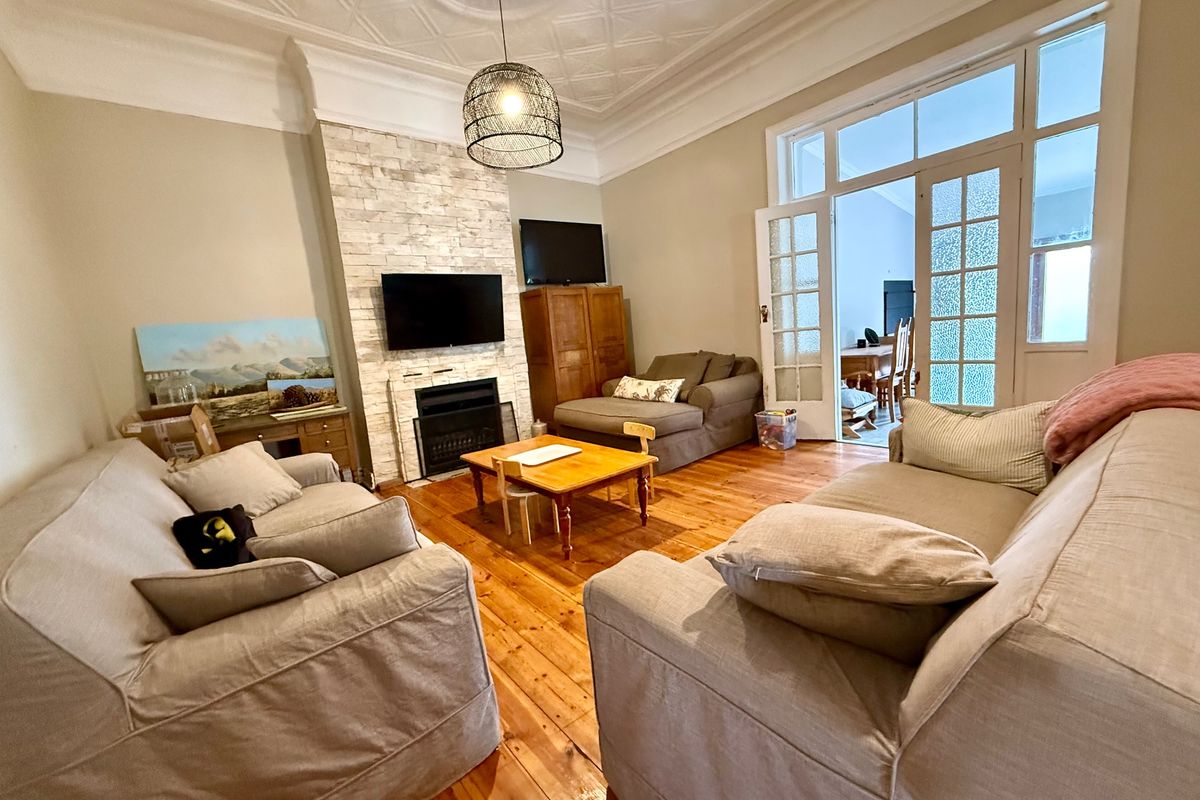 A spacious living room featuring original hardwood floors, a decorative pressed metal ceiling, and a stone-clad fireplace, with French doors leading to an adjoining space.