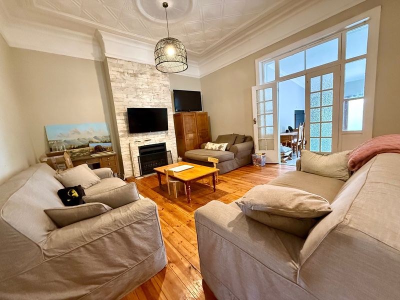 A spacious living room featuring original hardwood floors, a decorative pressed metal ceiling, and a stone-clad fireplace, with French doors leading to an adjoining space.