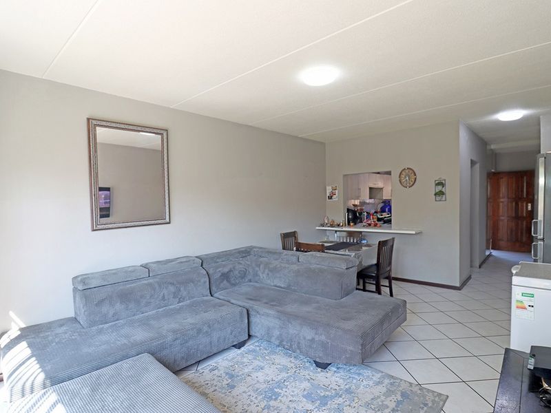 Open plan living area featuring tiled flooring, a pass-through kitchen window with a breakfast counter, and neutral wall finishes.