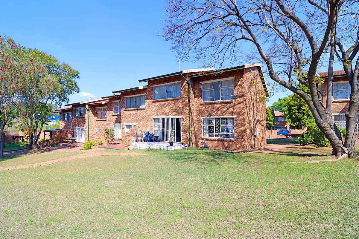 Rear view of a multi-story face brick apartment building featuring a paved patio area and surrounding lawn.