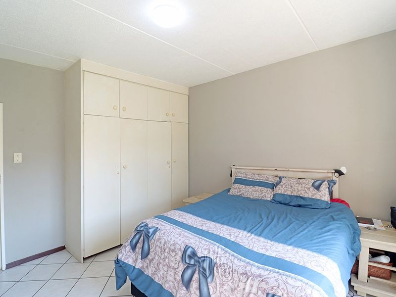 A functional bedroom featuring built-in cupboards, tiled flooring, and neutral wall tones, offering a practical space ready for personal updates.