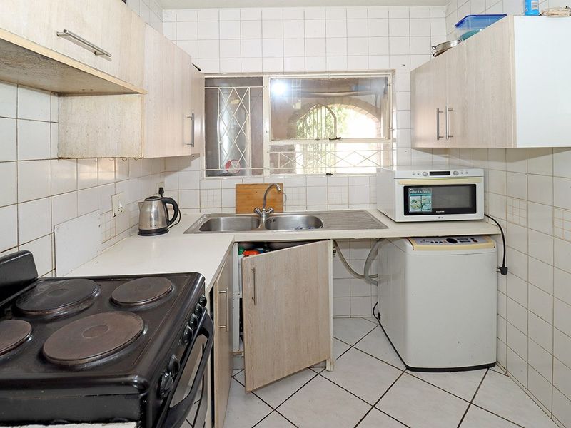 Compact kitchen featuring laminate cabinetry, tiled splashbacks, double bowl sink, and tiled flooring, requiring cosmetic updates to modernize the space.