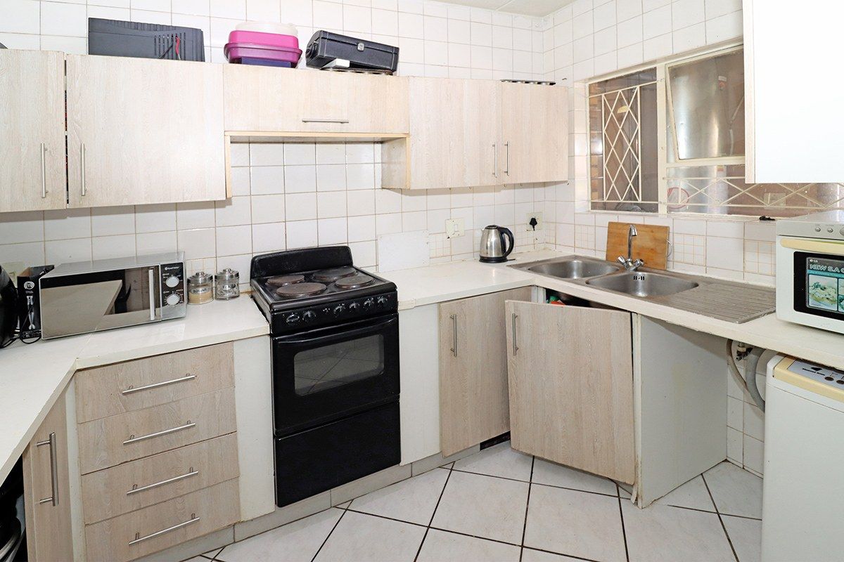 A functional kitchen featuring light wood-finish cabinetry, tiled backsplash, double stainless steel sink, and tiled flooring, requiring minor maintenance to cabinet hardware.