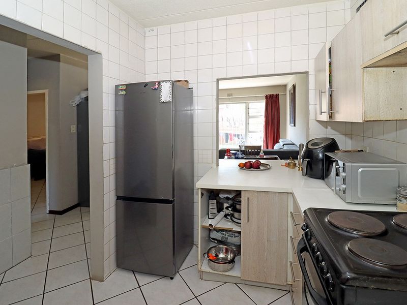 A functional kitchen featuring tiled walls and floors, built-in cabinetry, and a convenient pass-through window connecting to the living area.