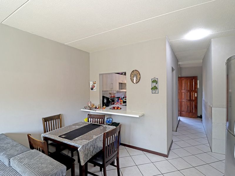 Open plan living area featuring a breakfast bar pass-through to the kitchen, tiled flooring, and access to a hallway with a solid wood door.