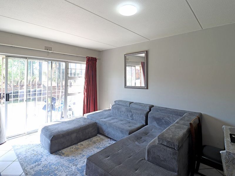 A living room featuring tiled flooring, a flush mount ceiling light, and a large sliding glass door with an integrated security gate.